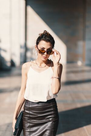 Beautiful, refined business woman holding fashionable sunglasses down looking above them on light blurred wall background in perspectiveの写真素材