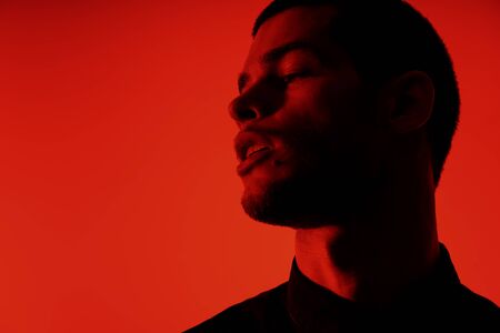 Silhouette of a young confident handsome businessman wearing black shirt in red light. Studio shot...