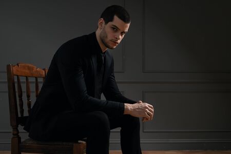 Young handsome businessman in black shirt and black suit. Confident young businessman posing on gray...