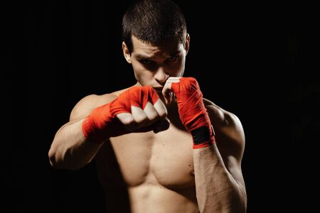 Athletic boxer punching with determination and precaution over black background. Strength, attack and motion concept. Fit caucasian model in movementの写真素材