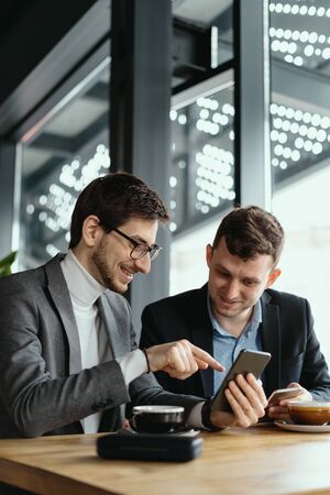 One-on-one meeting. Two young business people sitting at table in restaurant having a conversation using a phone and having a coffee