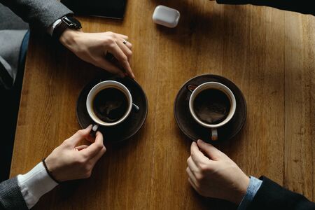 Top view two men hands gesticulating while holding cups of coffee on a wooden table backgroundの写真素材