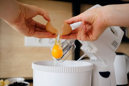 Close up woman hands break chicken eggs in a mixer bowl in the kitchen. Cooking dough.