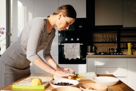 A woman rolls out the dough with a rolling pin with her hands for a delicious cake on a wooden table background on a sunny warm day.の写真素材
