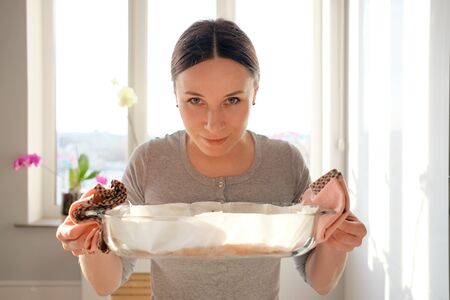 Young smiling woman enjoying the aroma of a freshly baked cake, with window in the background and sun rays covering the faceの写真素材