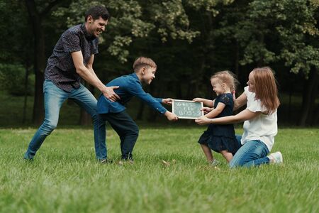 Competition between two teams, father and son and mother and daughter. Family having fun holding a board with the inscription, Who is the bossの写真素材