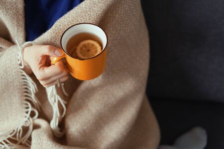 Woman's hand holding a yellow cup of tea with lemon on a cold day. Comfy moments, wool blanketの写真素材