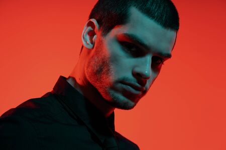 Portrait of a young confident handsome businessman in blue and red light. Studio shot on red...