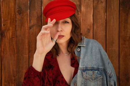 Close up portrait fashionable woman with wavy hair in red cap, active hands on wood background