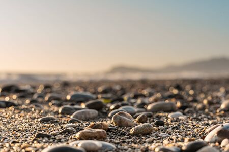 Close-up of pebble beach with light reflecting on stones against the blurred skyの写真素材
