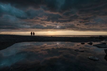 Silhouette of a fisherman fishing in sunset or sunrise time with clouds reflecting in to the waterの写真素材