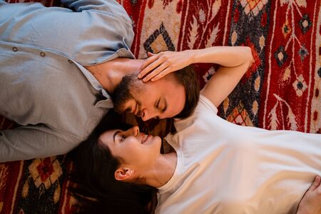 Top view young charming couple looking to each other smiling while lying on a colorful carpet with...