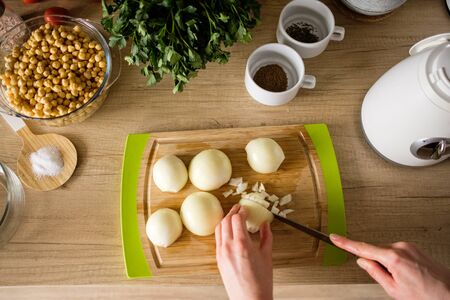 Woman hands, cutting onions, dill while preparing ingredients for falafel. Healthy diet
