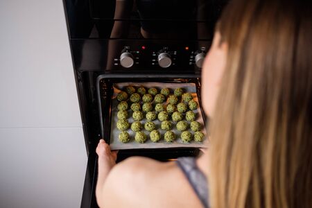 Beautiful woman put in the oven raw falafel arranged on baking paper in the tray. Healthy food diet, vegan backgroundの写真素材