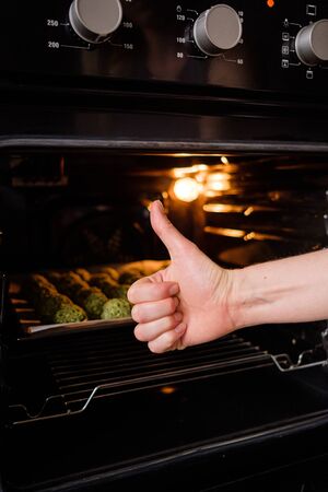 Raw falafel arranged on baking paper in the tray in oven. Healthy food diet, vegan background. Hand showing ok signの写真素材