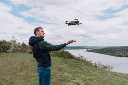 Young man piloting drone outdoor in nature. Guy testing aerial unmanned vehicle at nature. Backdrop...