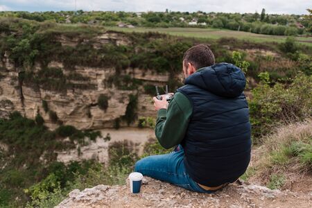 Young man piloting drone outdoor in nature. Guy testing aerial unmanned vehicle at nature. Backdrop...