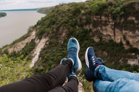 Man and women legs, sit together beside the lake or river in front of mountain and lake viewsの写真素材