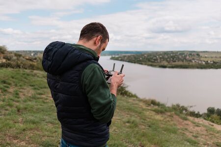 Young man piloting drone outdoor in nature. Guy testing aerial unmanned vehicle at nature. Backdrop...