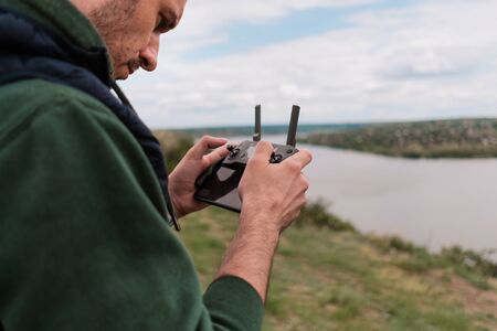 Young man piloting drone outdoor in nature. Guy testing aerial unmanned vehicle at nature. Backdrop for adult entertainmentの写真素材