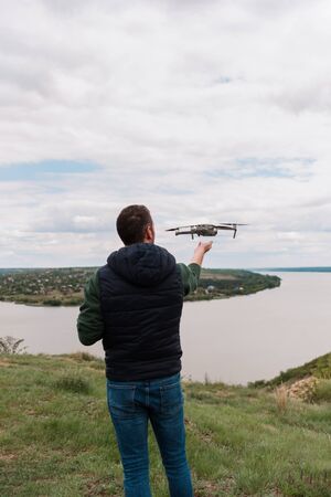 Young man piloting drone outdoor in nature. Guy testing aerial unmanned vehicle at nature. Backdrop...
