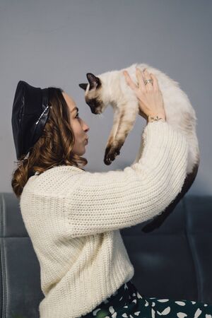 Lovely woman playing with Siamese cat at home. Friendship between humans and animalsの写真素材