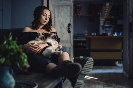 Attractive girl embracing her Siamese cats. Indoor portrait of cute woman playing with her two pets.