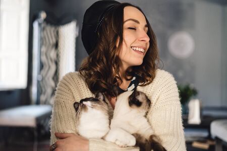 Attractive girl embracing her Siamese cats. Indoor portrait of cute woman playing with her two pets.の写真素材