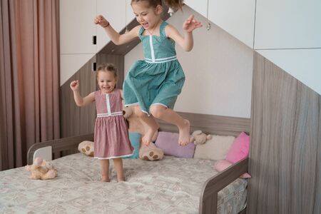 Happy funny little girls in motion jumping on bed alone flying in air feeling joy, cheerful cute active kid having fun playing laughing in bedroomの写真素材