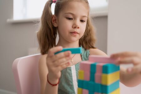 Little girl with a lovely friendly face playing with colored blocks in a creative educational game as she stands at pink tableの写真素材