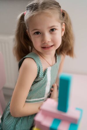 Little girl with a lovely friendly face playing with colored blocks in a creative educational game as she stands at pink tableの写真素材