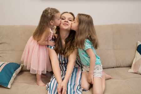 Lovely little daughters kissing sweet their sunny mother on checks. Happy family concept