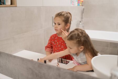 Lovely little girls applying makeup using the bath mirror, they want to be beautiful like mama.