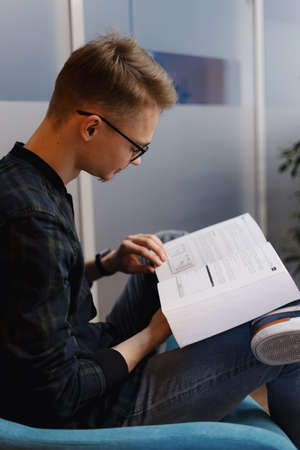 Young professional with glasses study Java coding while sitting in a blue armchair in the officeの写真素材