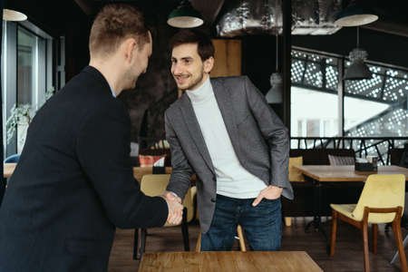 Smiling young business partners in business casual wear looking at each other while shaking hands after agreement. Greeting conceptの写真素材