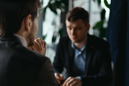 Focused businessman listening to business partner talking during discussion, thinking over his ideas while sitting at the tableの写真素材