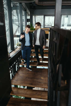 Two men walking down on wooden stairs chatting indoors. Communication concept