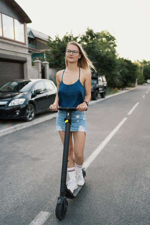 Young beautiful girl riding an electric scooter in the summer on the street