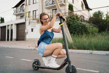 Young beautiful girl riding an electric scooter in the summer on the streetの写真素材