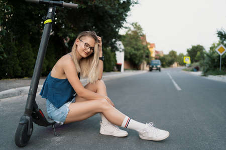 Young beautiful girl is sitting on her electro scooter in the summer on the streetの写真素材