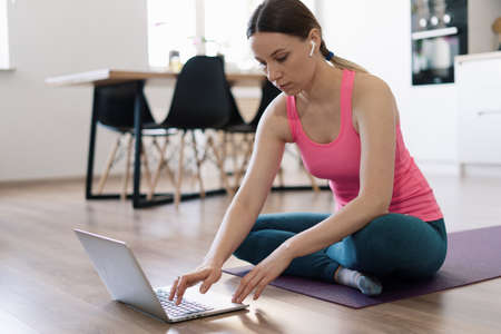 Attractive woman practicing yoga at home using online training instructions