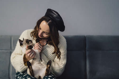 Lovely woman playing with Siamese cat at home. Friendship between humans and animalsの写真素材