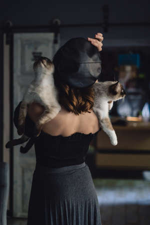 Back view portrait of woman with two siamese cats on her bare back. Female wears black beret indoors.の写真素材
