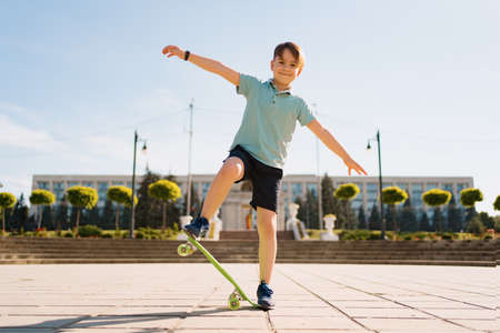 Happy young boy playing on skateboard in the park, Caucasian kid riding penny board, practicing skateboard.の写真素材