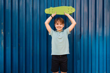 Portrait Young cool smiling BOY in blue polo posing with PENNY BOARD in the hands on a blue...