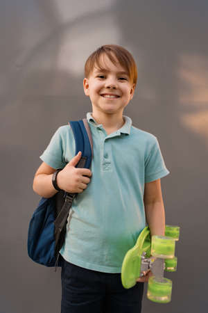 Young SCHOOL BOY with backpack posing with PENNY BOARD in the hands on gray backgroundの写真素材