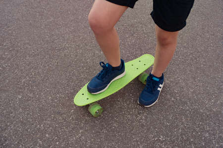 Close up legs in blue sneakers riding on green skateboard in motion. Active urban lifestyle of...