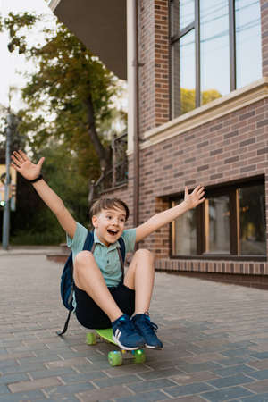 Happy young boy playing on skateboard in the city, Caucasian kid riding penny board on buildings...