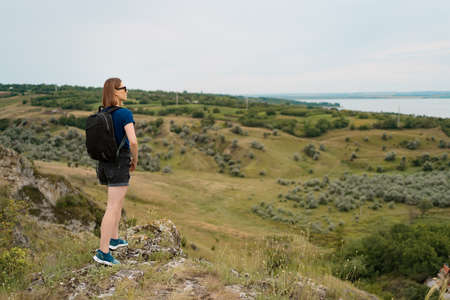 Young woman with backpack standing on cliffs edge and looking to the sky and beautiful nature....