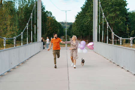 Cheerful lovely couple running happy on bridge with their dog and pink balloons smilingの写真素材